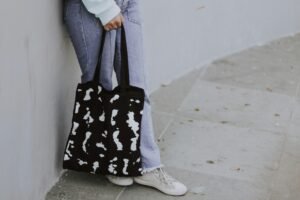 A person in jeans holding a black and white tote bag outdoors.