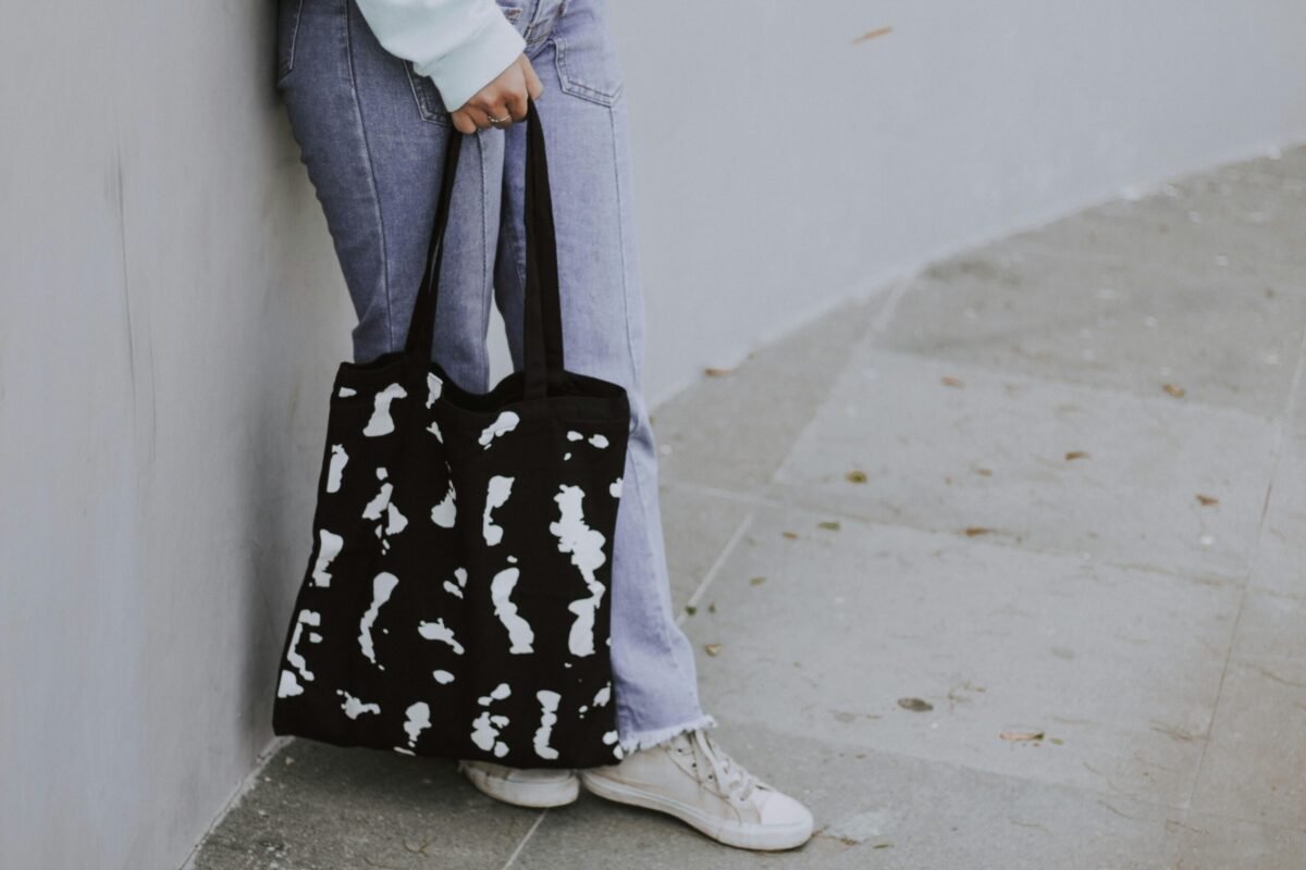 A person in jeans holding a black and white tote bag outdoors.