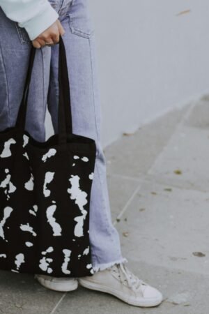 A person in jeans holding a black and white tote bag outdoors.